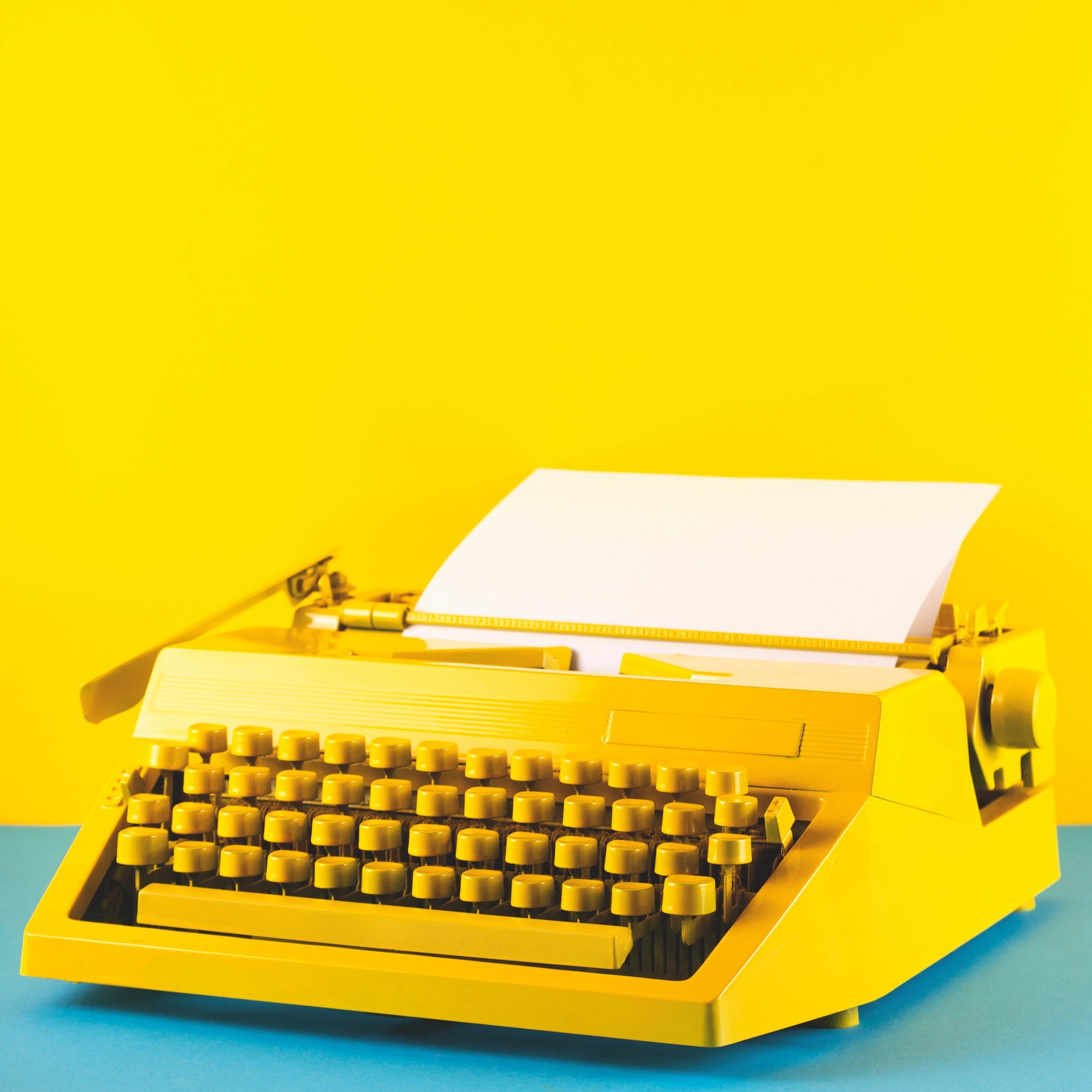 Yellow typewriter on blue table. Creativity and copyright concept